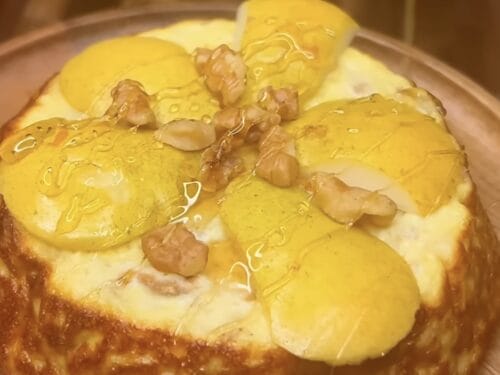 Baked custard tart topped with poached pear halves, nuts, and glossy yellow sauce in shallow bowl